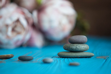 Pyramids of gray zen pebble meditation stones with green leaves and beautiful fresh peony flowers on wooden background. Concept of harmony, balance and meditation, spa, massage, relax