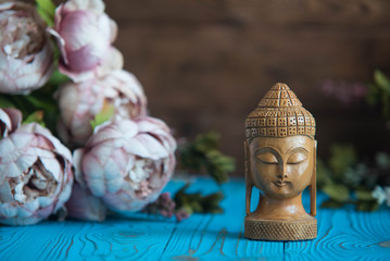 Buddha statue with beautiful fresh peony flowes on wooden background. Concept of harmony, balance and meditation, spa, massage, relax
