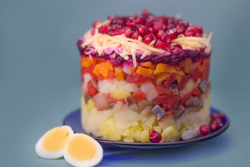 The dish is prepared in layers of salted herring, potatoes, beets, carrots, eggs and pomegranate berries on a blue background.