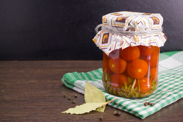 Salted tomatoes in a glass jar prepared for the winter and Bay leaf and black pepper on a green white napkin.