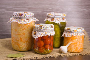 Pickles, salted tomatoes, salted cabbage in glass jars on a wooden background.