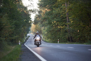 Bearded biker in sunglasses, helmet and black leather clothing riding modern powerful high-speed...