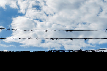 black barbed wire against the sky with clouds. Barbed wire on the black fence against cloudy sky. conceptual photo that displays unfreedom.