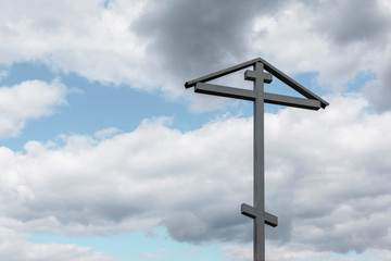 gray orthodox cross on a blue sky background with gray clouds. Ancient cross on background of  blue sky. Orthodox cross