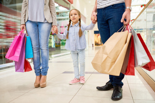 Portrait of happy family shopping in mall, focus on cute little girl holding hands with parents