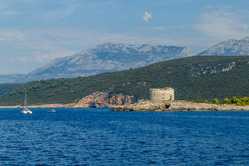 Stony seashore, mountains on the horizon and the old round fortress