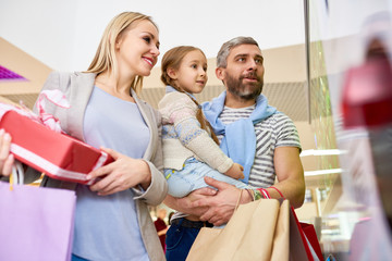 From below of casual parents with little daughter looking at window in mall having holiday shopping