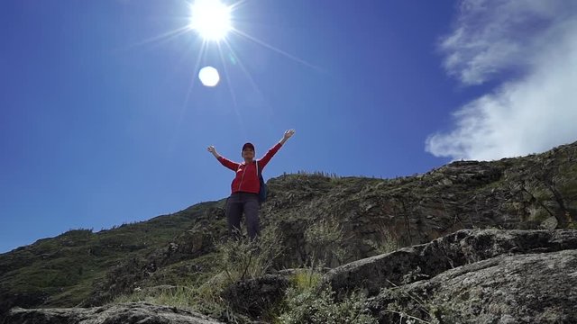 Young happy torist woman with backpack and cap reached up top of mountain and put his hands in the air. Front view, slider