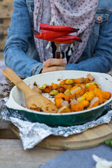 Woman hands take with fork baked, roasted, grilled vegetables in white cast iron skillet, pan with spices and herbs. Red bell pepper, pumpkin, potato, zucchini, Vegan, vegetarian healthy food
