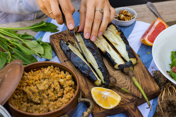 Woman hands cut with knife roasted, grilled, baked eggplants on wooden cutting board. Vegan vegetarian healthy food, paleo diet. Vegetables