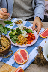 Hand put, add vegetables to buddha bowl plate with red pepper bell salad, cooked vegetables (broccoli, brussels sprouts, cauliflower), spinach, grapefruit, Indian lentil. Vegan vegetarian healthy food