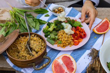 Hand put, add vegetables to buddha bowl plate with red pepper bell salad, cooked vegetables (broccoli, brussels sprouts, cauliflower), spinach, grapefruit, Indian lentil. Vegan vegetarian healthy food