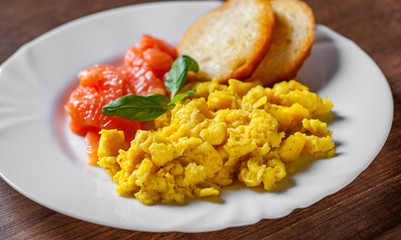 Scrambled eggs with smoked salmon and toast in white plate on wooden table background