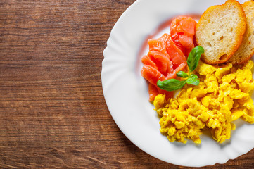 Scrambled eggs with smoked salmon and toast in white plate on wooden table background