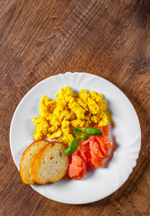 Scrambled eggs with smoked salmon and toast in white plate on wooden table background