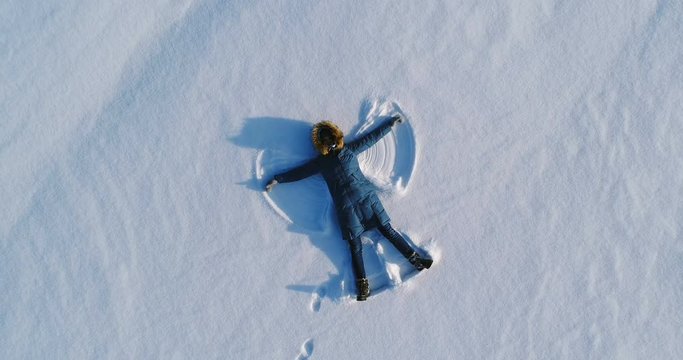 Woman Makes Snow Angel Laying In The Snow. Aerial Video. Camera Moves Away Slowly.