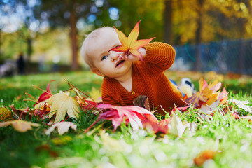 Baby girl playing with colorful autumn leaves outdoors