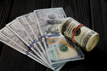 A thick roll of old hundred dollar banknotes tied a red rubber band lies on the whisker of new hundred dollar bills