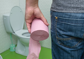 A roll of toilet paper in the hand of a man near the toilet. Diarrhea or indigestion, concept