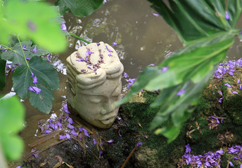 Buddha head surrounded by purple flowers and green leafs. - Powered by Adobe