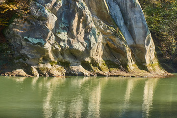 A fragment of a rock (called a cockerel) is reflected in the clear water of a mountain river on a sunny day. Close-up of a fragment of rock. Autumn landscape with mountain river and rock