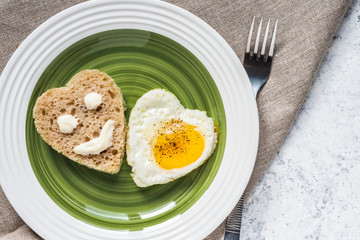Fried egg and bread in the shape of a heart. Smiley on a piece of bread.