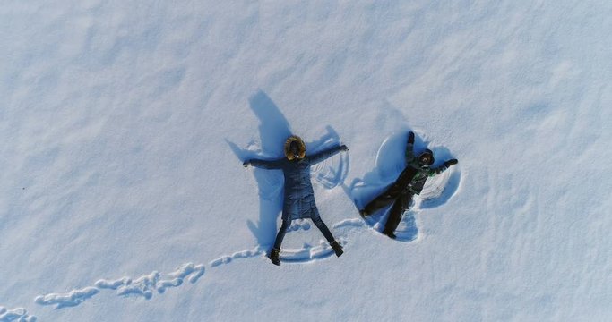 Mom and son make snow angels together. Camera slowly rising. Aerial footage.