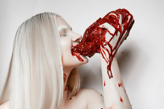 A young girl soiled in blood bites fresh meat.