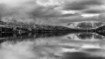 Beautiful reflection in the Tyrifjorden (Lake Tyri) after a rainy day in Norway. Dramatic sky, fog, trees and mountains are perfectly mirrored in the lake. Black and white picture