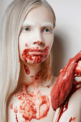 A girl soiled in blood holds a piece of fresh meat in her hands.