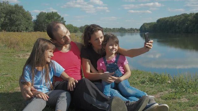 Family is photographed on a smartphone. Parents with daughters in nature are photographed.