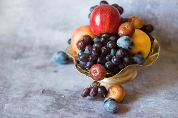  Assortment of fruits in a metal plate on a gray background. Serving natural fresh fruits and...