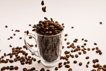 Grains of coffee are poured into a glass cup on a white background