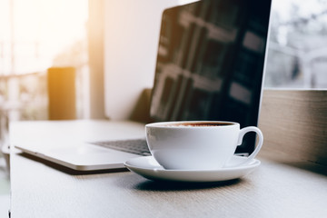 Coffee cup and laptop on desk bar in cafe with drink in morning.