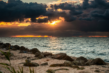 Cloudy sunset over a lake with rainy dark storm clouds and sunbeams and sun harps