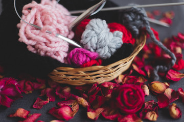 Knitting yarn and a ball of yarn in a straw basket. Dry petals and dried flowers. Concept of home, warm comfort in autumn, winter or spring. Top view, flat lay, background.