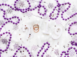 Christmas and New Year background with numbers 2019, wedding rings with diamond, violet decorations and light bulbs.