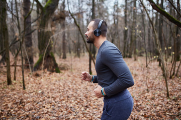 Athlete Jogging in the woods. A young man with headphones running in the woods.