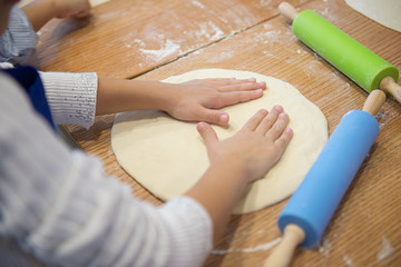 Hands of children rolling pizza dough with rolling pin on the kitchen table. Cooking pizza.