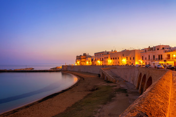 A view of the sea during sunrise in Gallipoli, Italy from the old wall in the city center with the street lights on