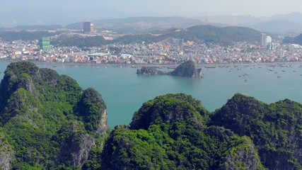 Fototapeta premium Aerial view on a coastal city in Halong Bay, with lime stone karsts isles overgrown by vegetation in the foreground. Hanoi, Vietnam. 10.02.2018