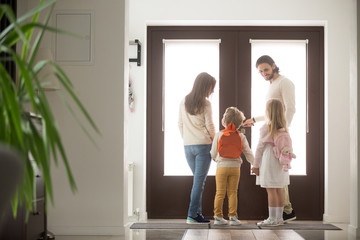 Married young couple with little preschool brother and sister standing in hallway near entrance door, gathering at school or for a walk. Happy wellbeing family spending free time or weekend together