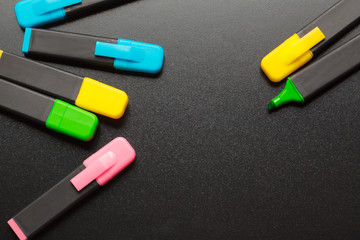 Several colorful highlighters on black desk background close up