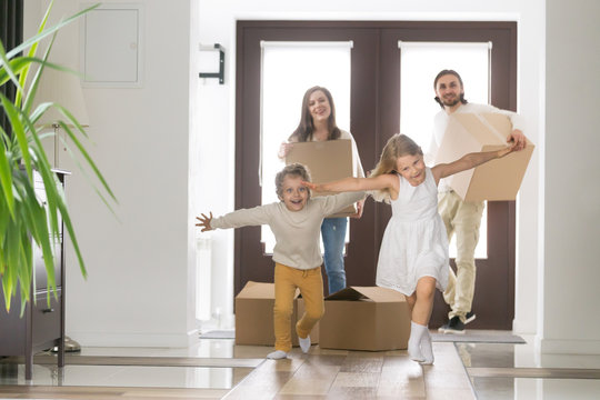 Happy married couple and little children arrive at new modern house. Husband and wife with cardboard boxes look at running inside excited daughter and son. Buy realestate, mortgage and moving concept