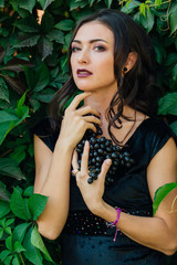 Portrait of young sexy brunette with black grapes.