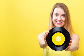 Young woman with a vintage vinyl record on a yellow background