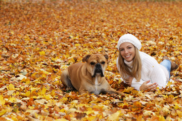 Happy woman with cute dog sitting in autumn leaves
