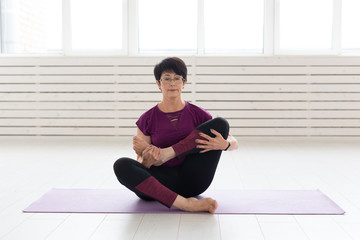 People, yoga, sport and healthcare concept - Attractive middle-aged woman stretching and sitting in yoga lotus position