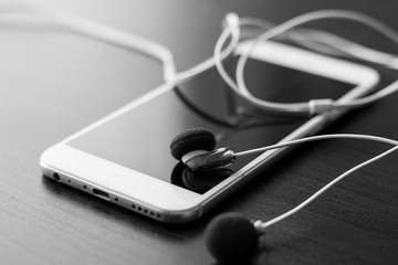 teléfono móvil blanco con auriculares sobre fondo negro