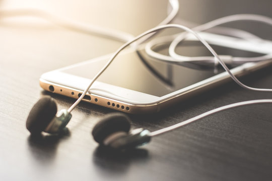 tel&eacute;fono m&oacute;vil con auriculares a contraluz sobre fondo negro